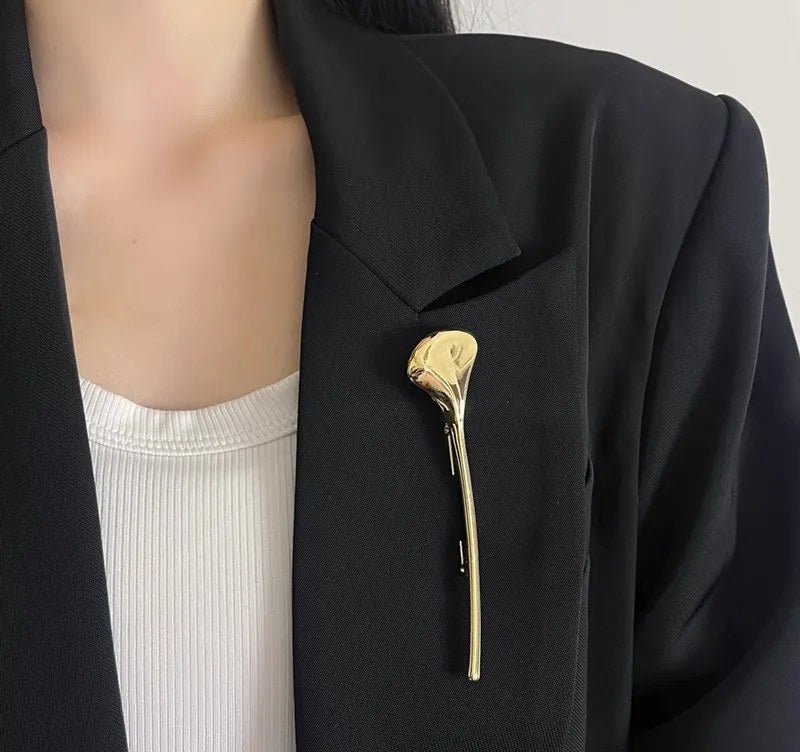 Gullfarget brosje formet som et ginkgoblad på en svart blazer