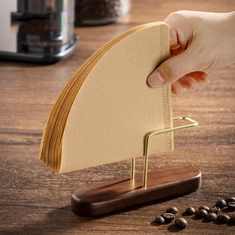 Kaffefilterholder i valnøtt med en bunke brune kaffefiltre i den gullfargede bøylen