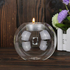 Rund telysholder i klart glass med tent telys foran blomster