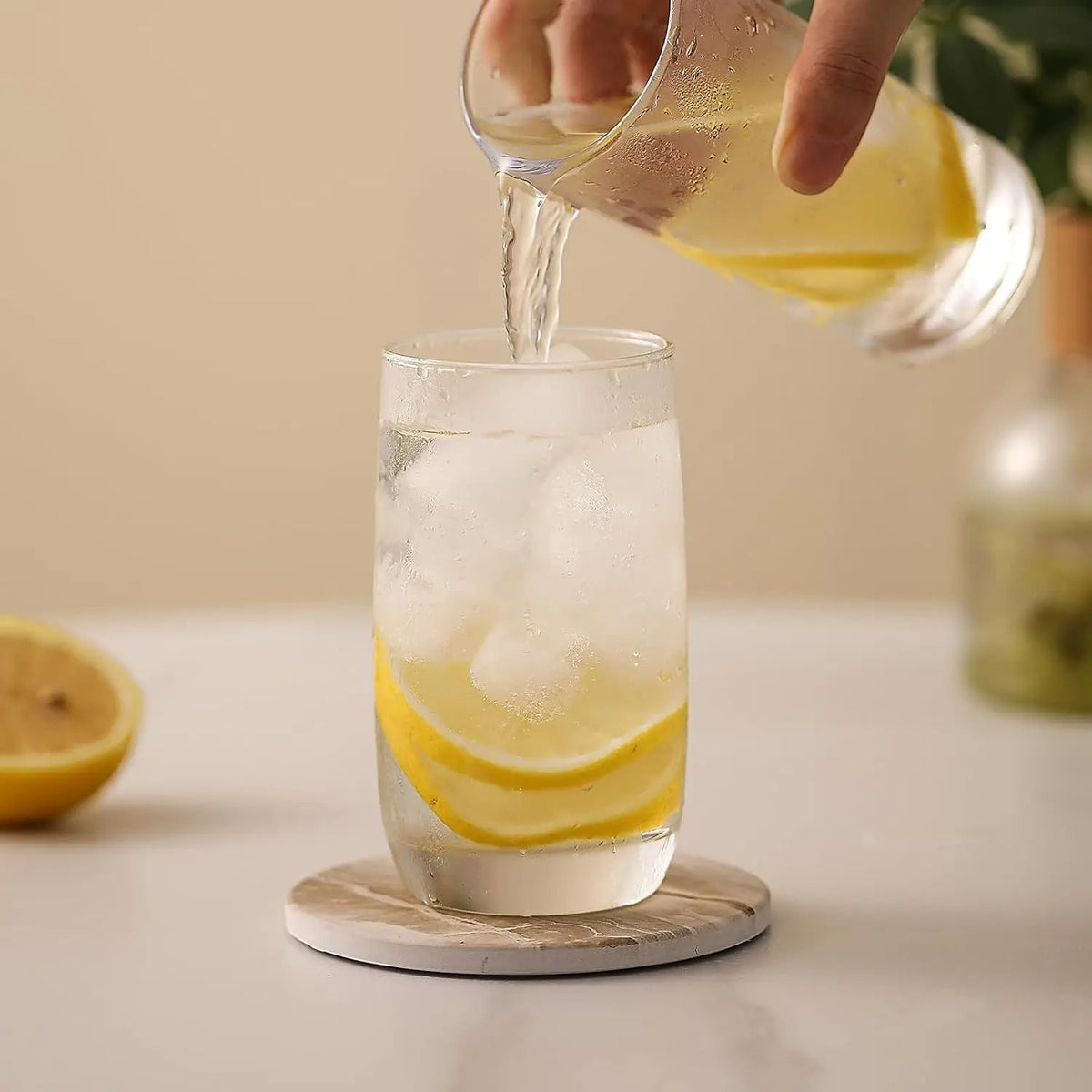 Et glass med is og sitron fylles mens det står på en glassbrikke med marmormønster