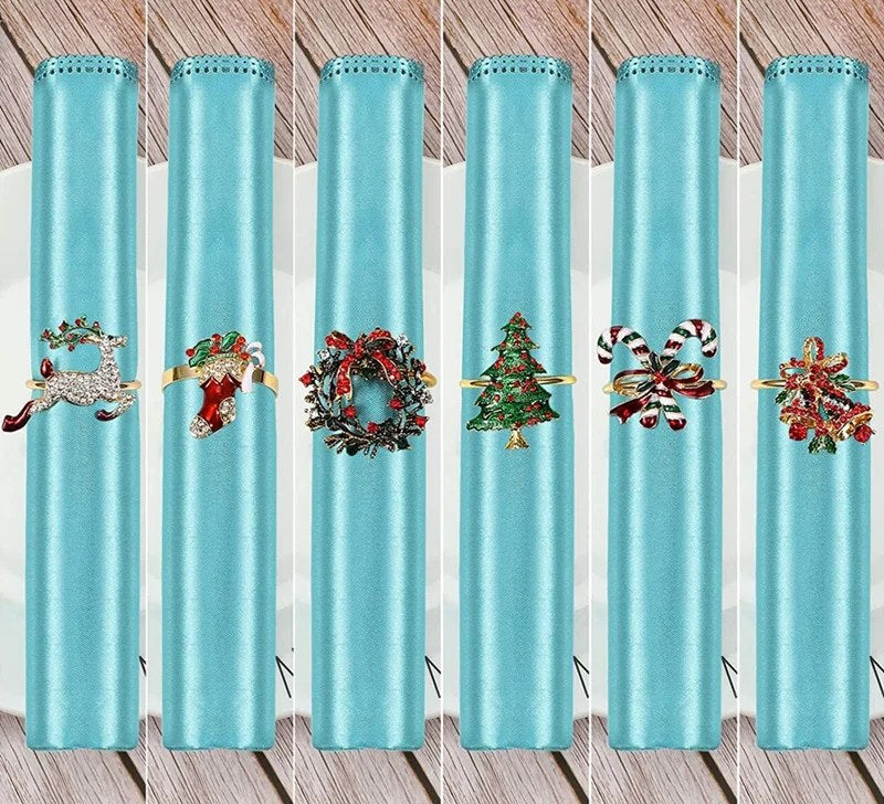 Seks rullede tøyservietter med hver sin serviettring: reinsdyr, julestrømpe, krans, juletre, sukkerstenger og bjeller