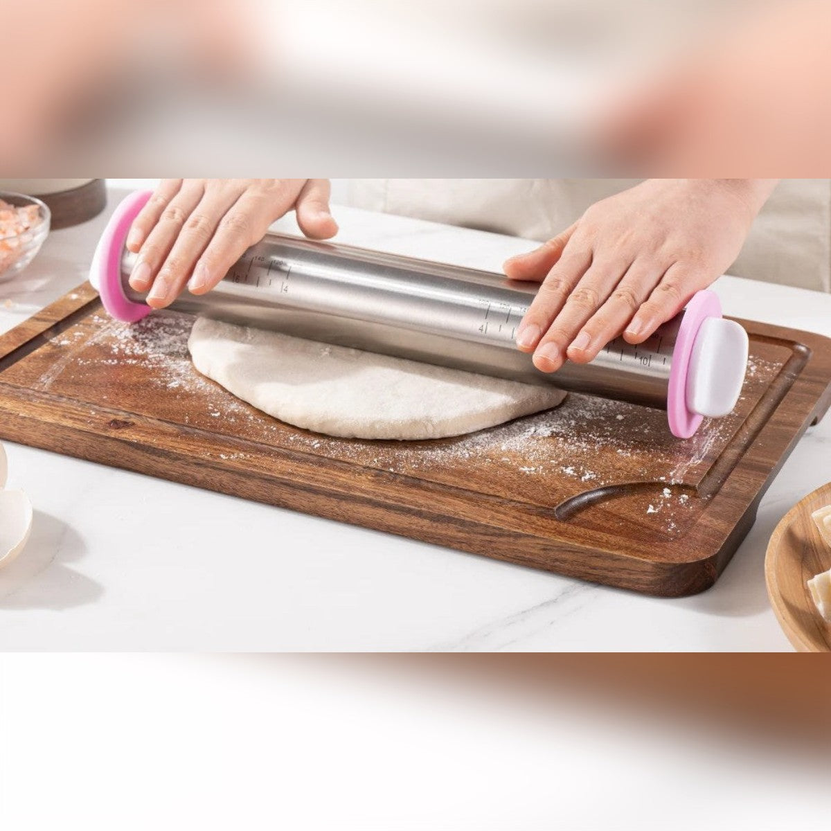 Kjevle i rustfritt stål med rosa ringer kjevler ut en deig på et skjærebrett