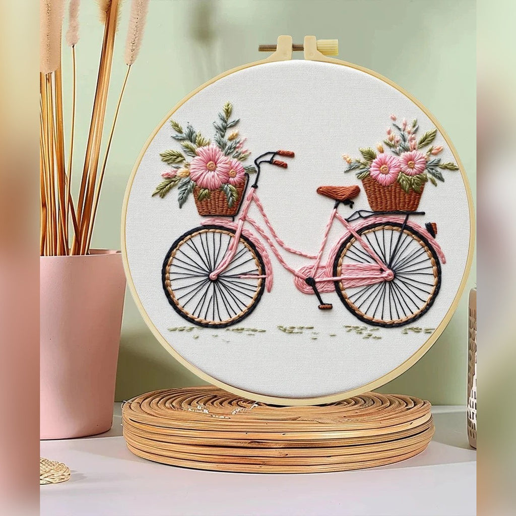 Broderisett med sykkel og blomsterkurver – det ferdige motivet i broderirammen på en hylle
