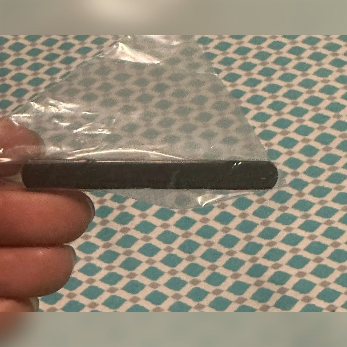Kundens bilde: svart slipsnål i en plastpose mellom fingrene