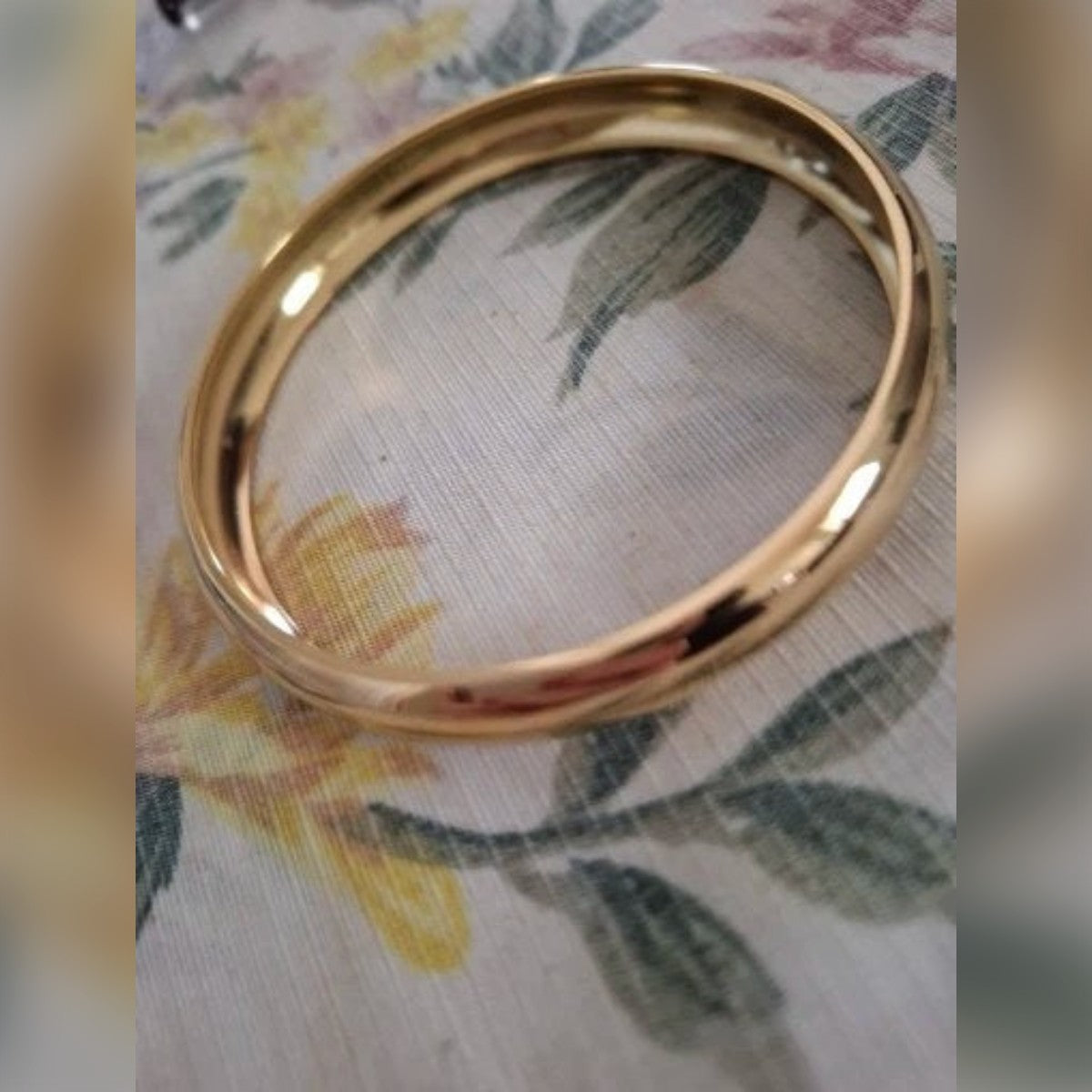 Kundens bilde: gullfarget armring på en blomstrete duk