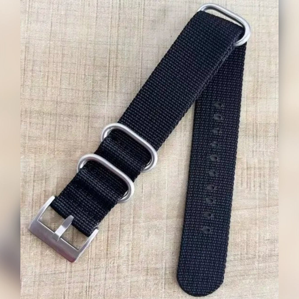 Kundens bilde: svart NATO strap med sølvfarget spenne og tre ringer på et trebord