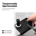 Svart tampermatte i hjørnemodell med kant ned over benkekanten, ca. 20 × 15 cm